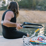 Person sitting on a dock, holding the black handle while the multicolored ski rope lays coiled nearby.