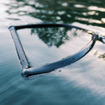 Black handle of the Ski Rope & Handle Combo floating on water, partially submerged with reflections.