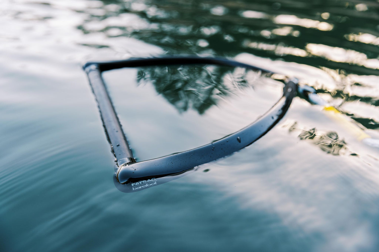 Black handle of the Ski Rope & Handle Combo floating on water, partially submerged with reflections.