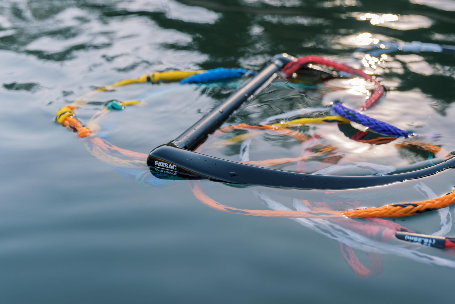 Black handle floating on water, surrounded by loops of multicolored ski rope.