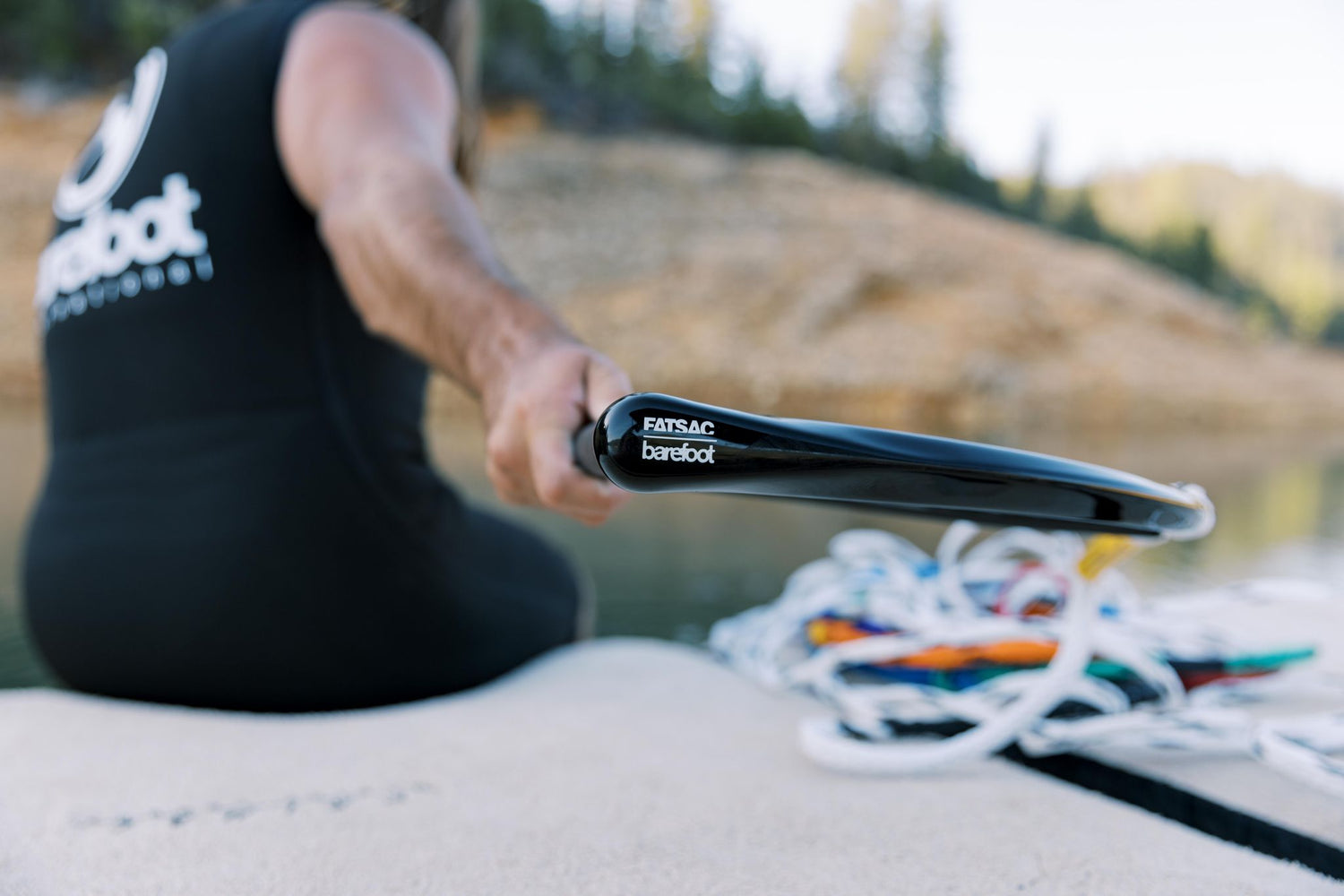 Close-up of a person holding a black handle with logo, multicolored rope coiled in the background.