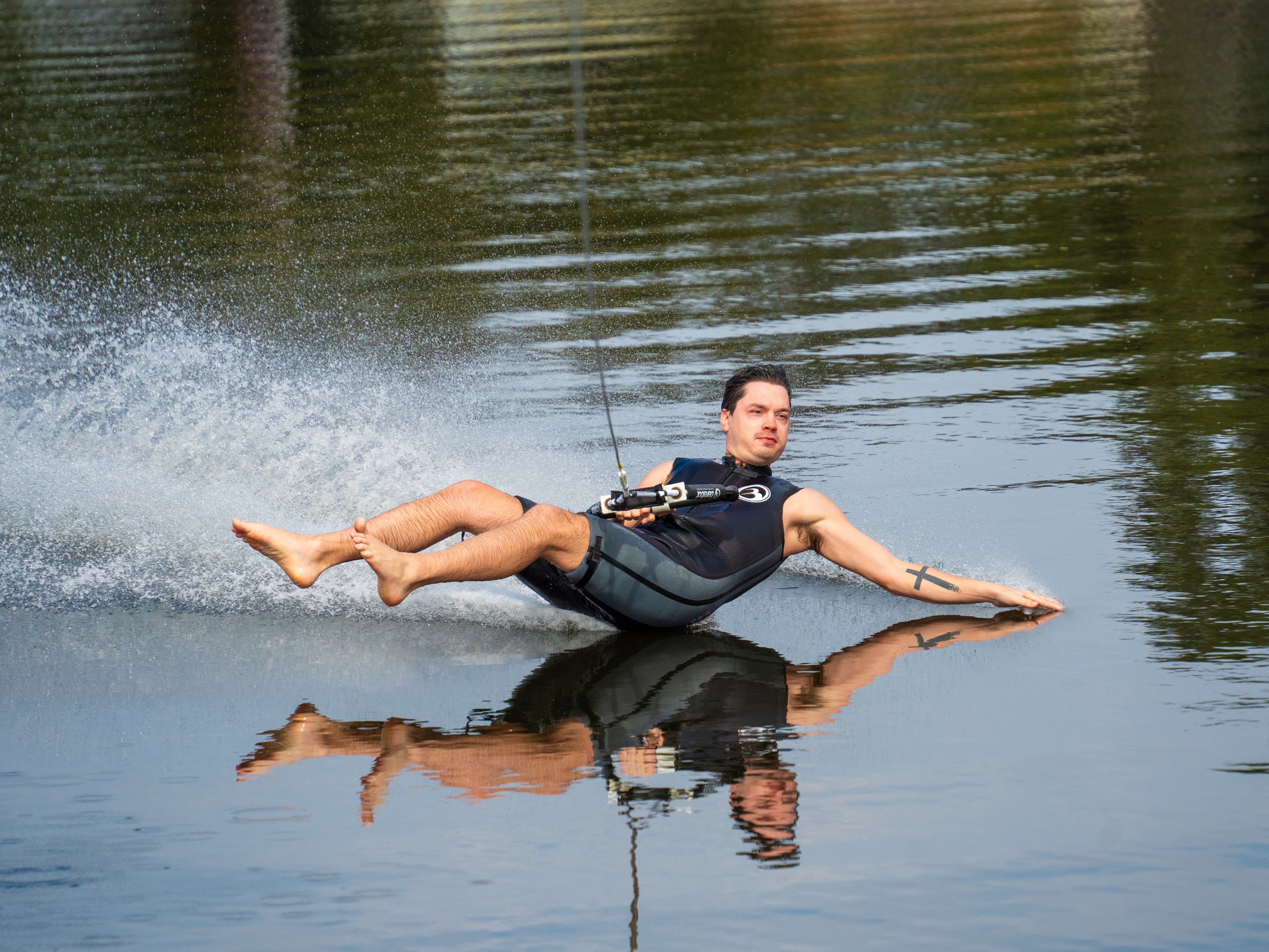 Barefoot waterskier leaning back while gliding smoothly across calm water, leaving a white spray.