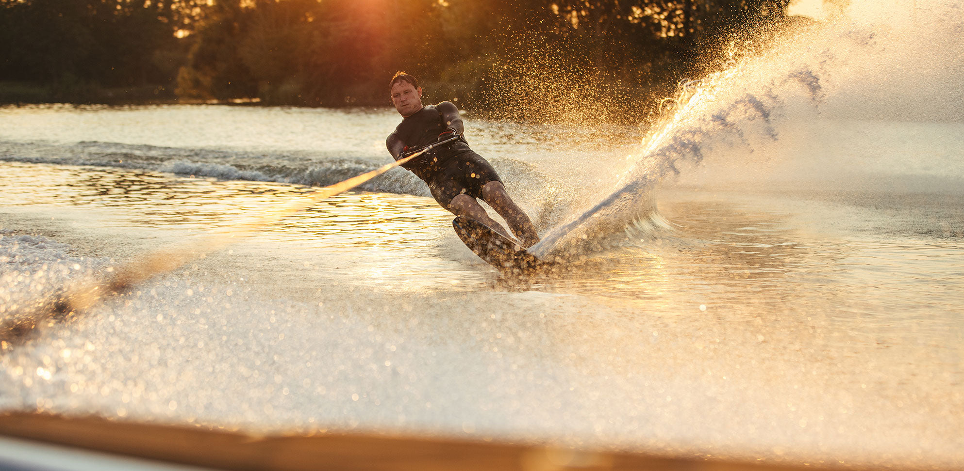 Slalom skier cutting through golden water at sunset, leaving a shimmering spray behind.