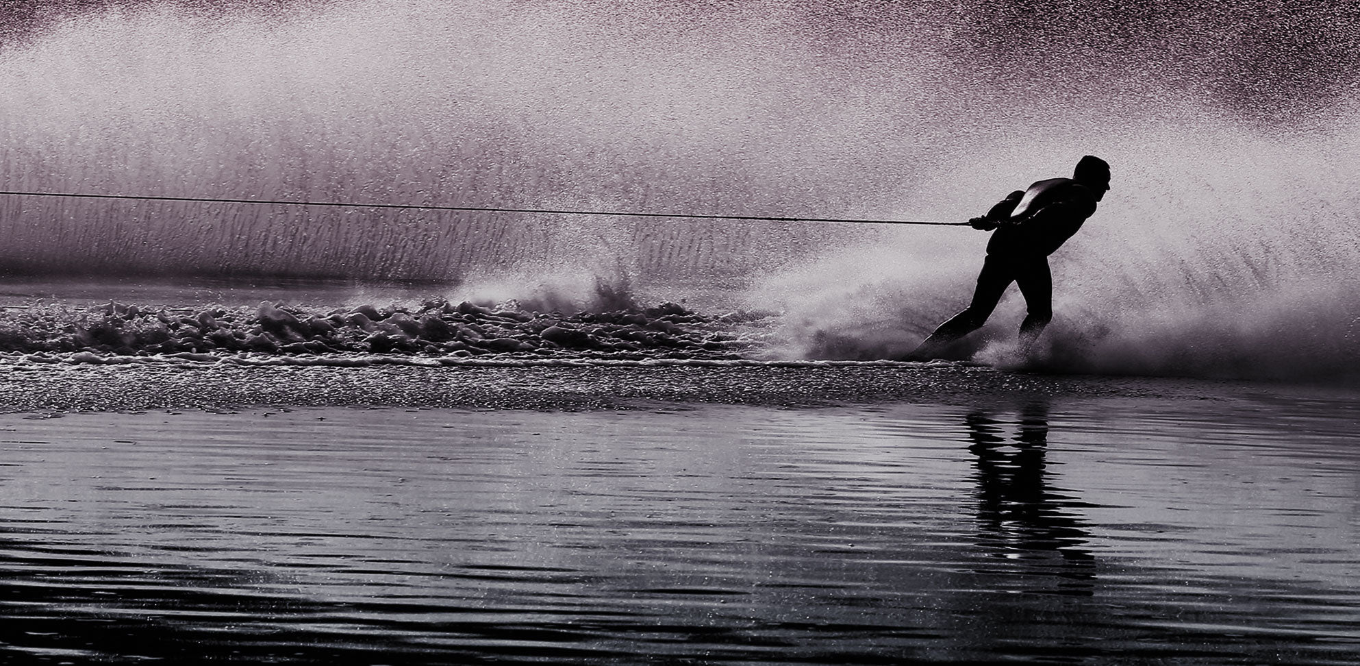High contrast photo of a waterskier carving sharply, leaving a dramatic spray of water behind.