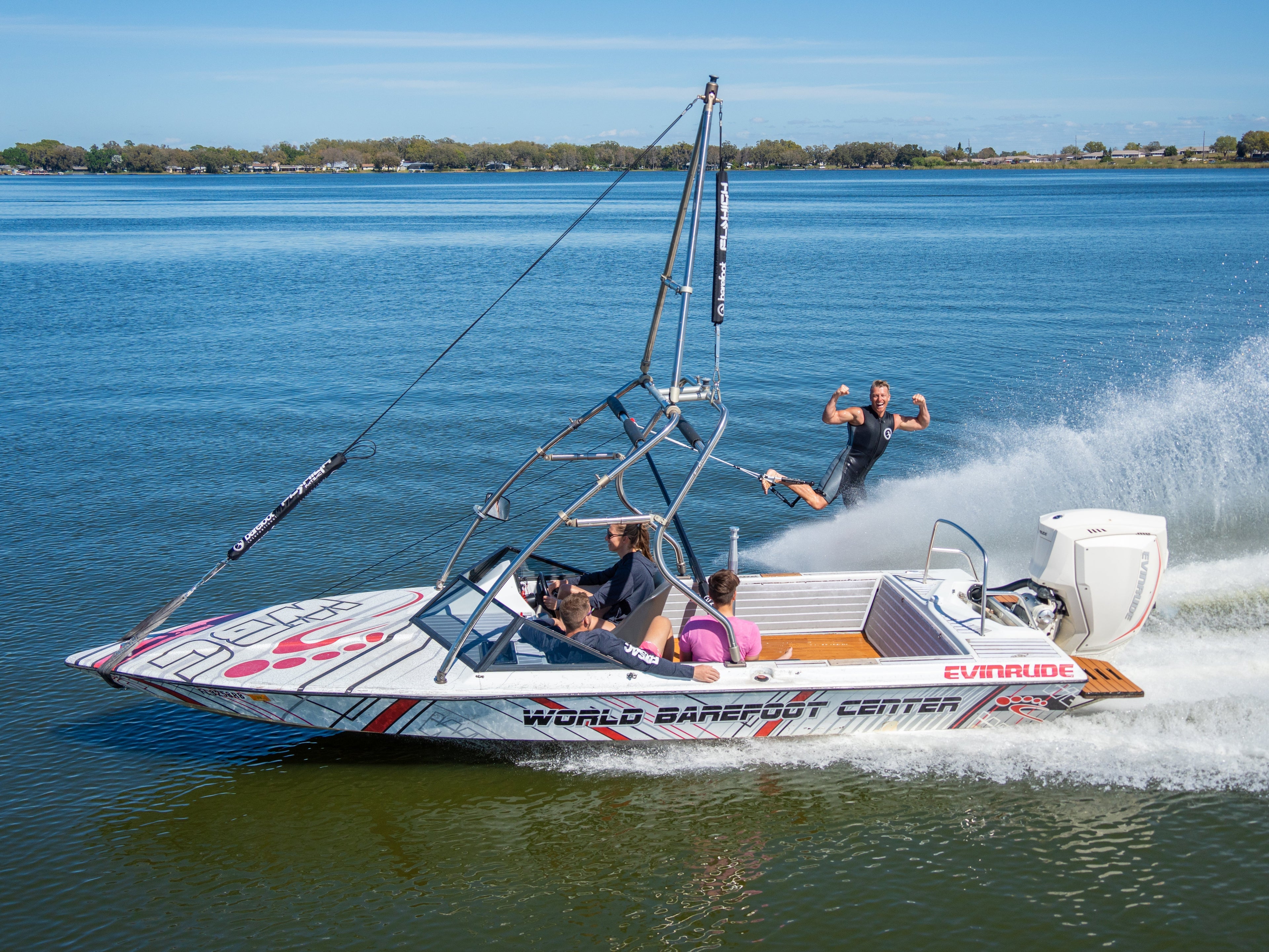 Barefoot waterskier being towed behind a World Barefoot Center boat, mid-air after launching from the wake.