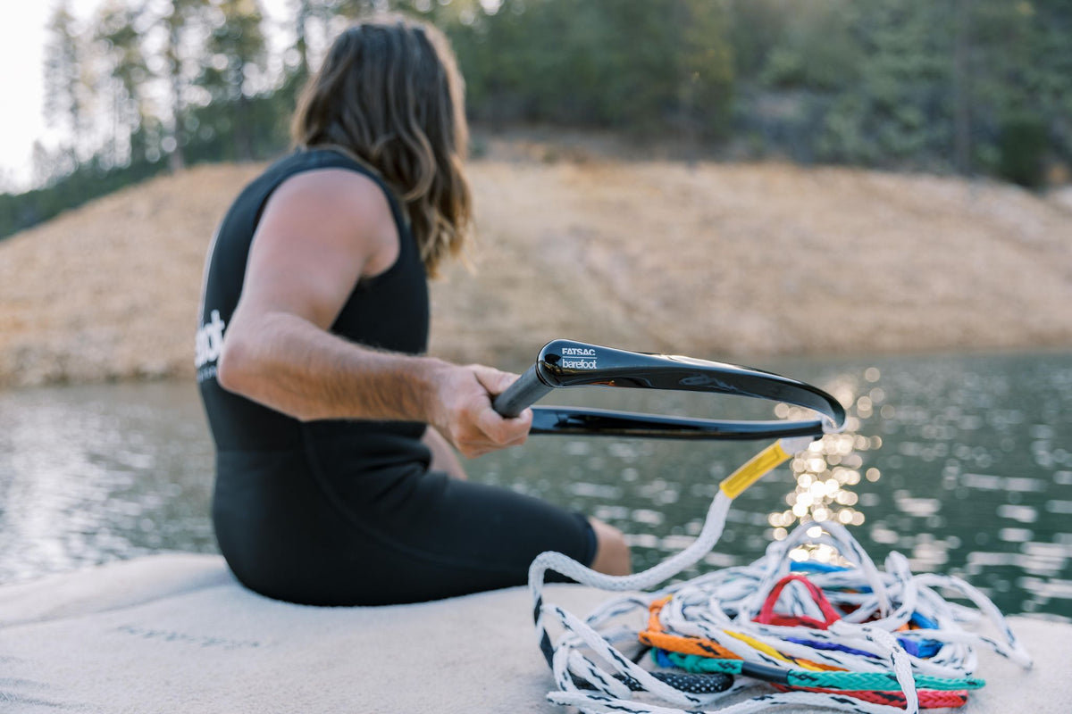 Person sitting on a dock, holding the black handle while the multicolored ski rope lays coiled nearby.