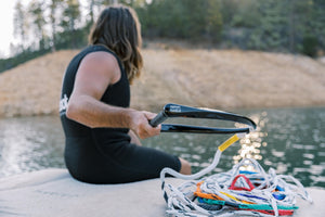 Person sitting on a dock, holding the black handle while the multicolored ski rope lays coiled nearby.