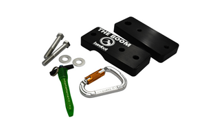 A black boom clamp box with "The Boom" text, a green quick-release pin, a silver carabiner, and mounting hardware.