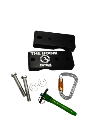 A top-view of a boom clamp box kit, including black metal plates, a green quick-release pin, a silver carabiner, and bolts.