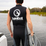 A man standing near the water wearing the Iron Sleeveless Wetsuit, holding a boom handle and coiled cable.