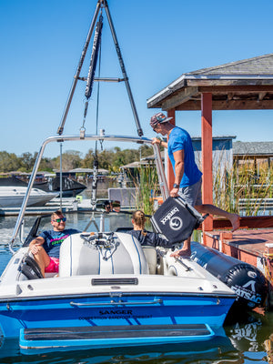 A blue and white Sanger Competition Barefoot Towboat at a dock with a barefoot boom setup and passengers onboard.