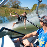 A barefoot waterskier in the Iron Short Sleeve Wetsuit riding on the water while holding a boom, with a boat driver watching.