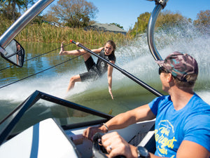 A barefoot waterskier in the Iron Short Sleeve Wetsuit riding on the water while holding a boom, with a boat driver watching.