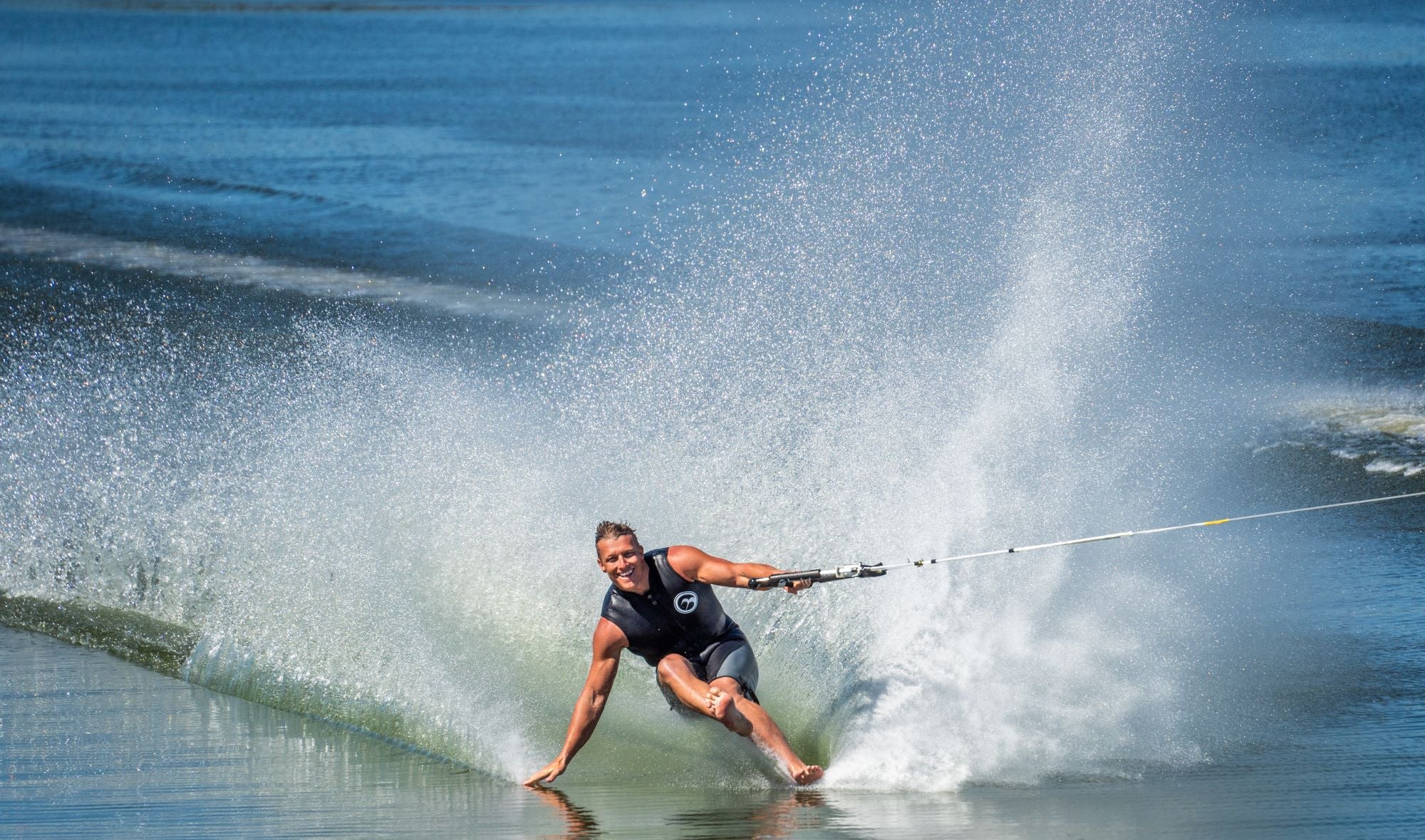 A barefoot water skier carving through the water, creating a large spray while holding onto a tow rope.