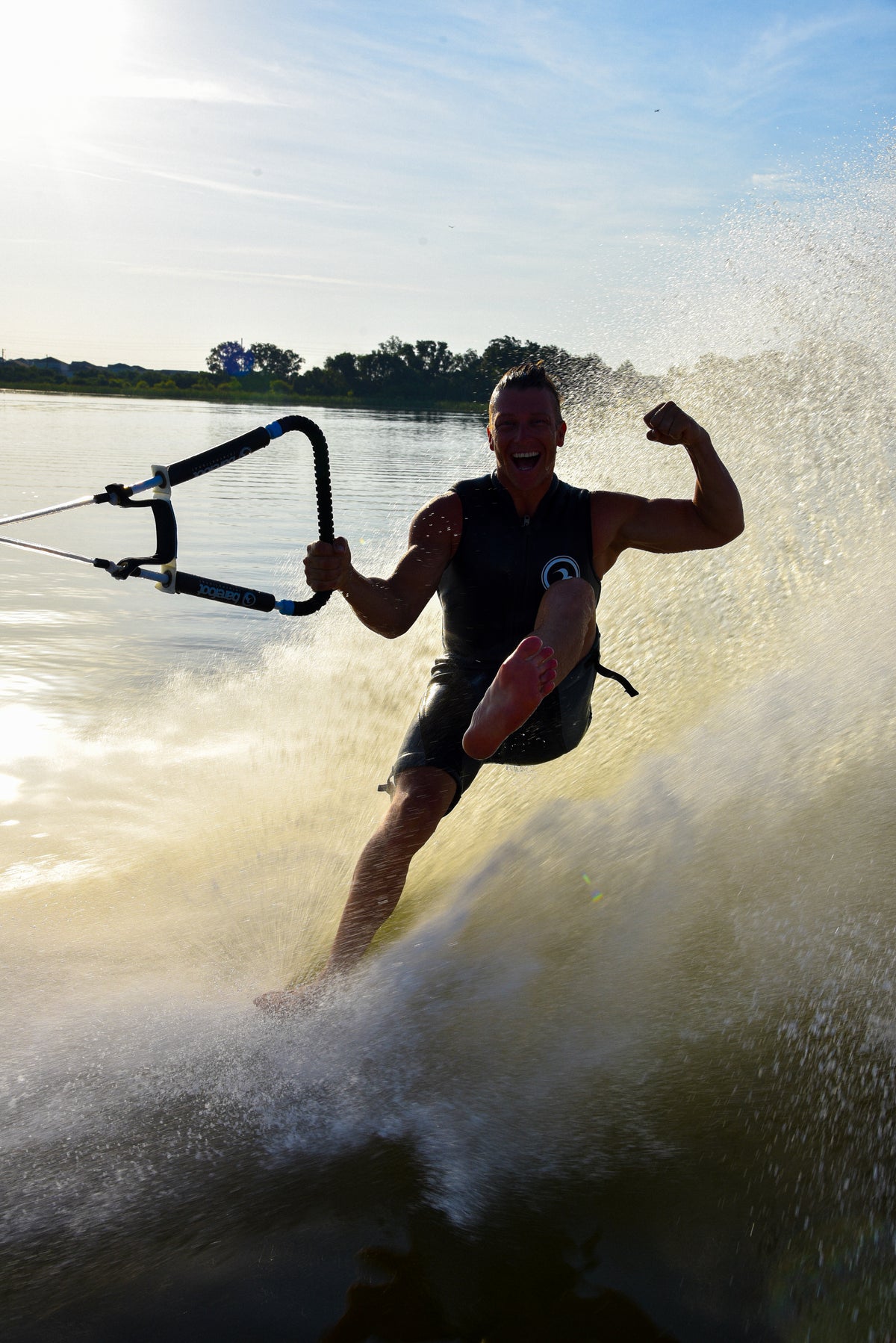 Person barefoot water skiing on a body of water flexing with a splash.