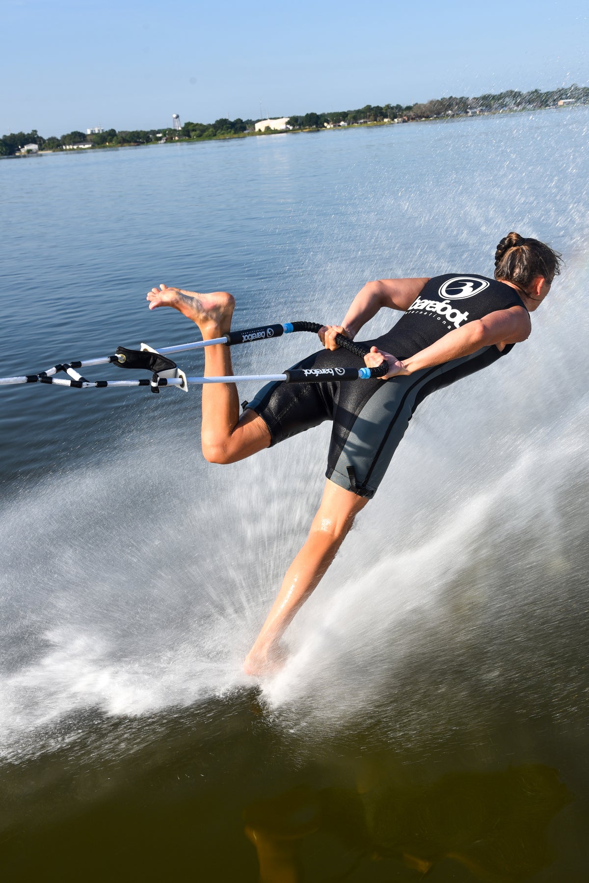 Person barefoot water skiing backwards on one foot on a lake with a clear sky