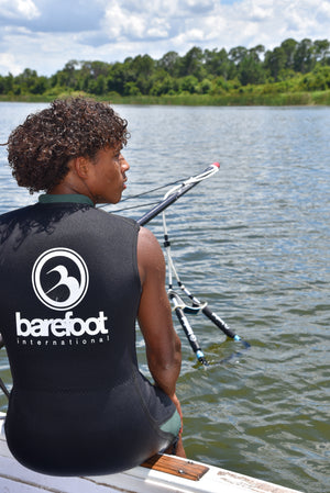 Man on a boat in a black Iron Sleeveless Wetsuit holding a boom bar over a lake.