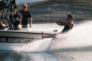 Man barefoot skiing behind a boat, holding the Wake Rope and T-Bar Handle as the crew watches.