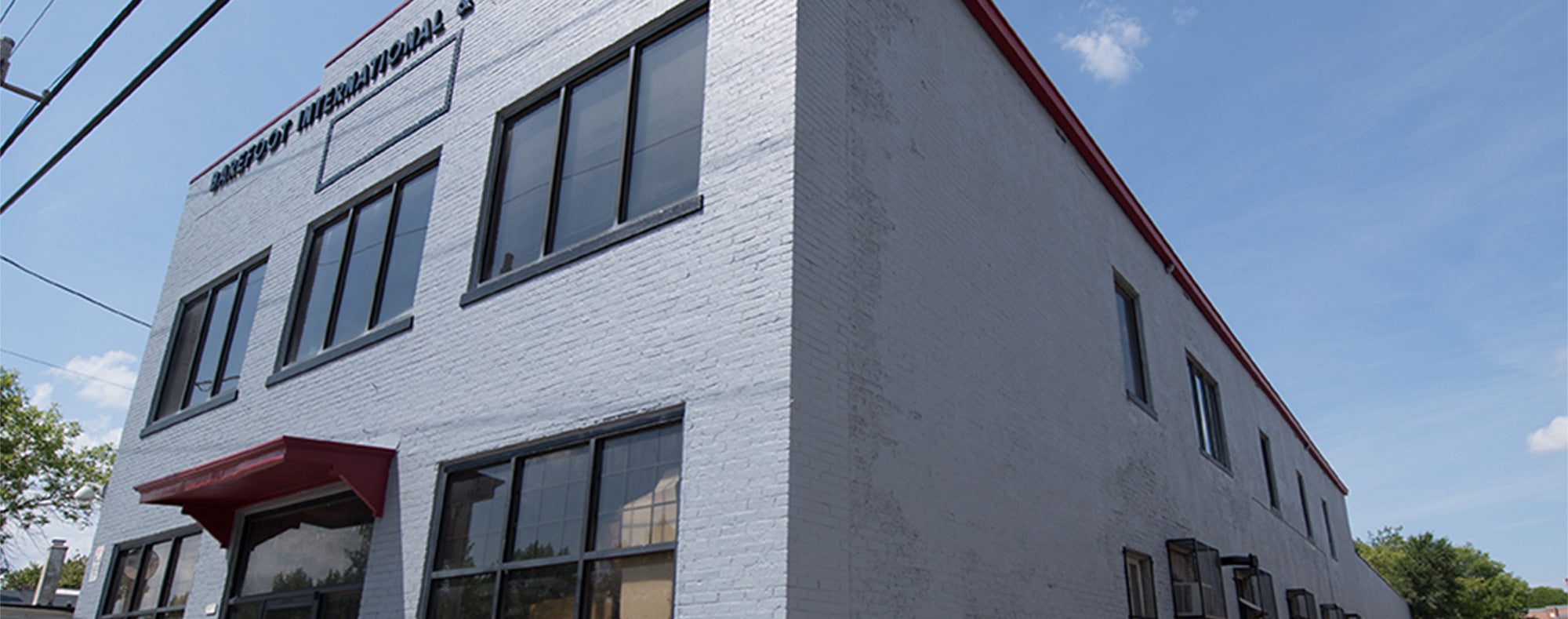 Barefoot International headquarters, a white brick building with black-framed windows and a red awning under a clear sky.