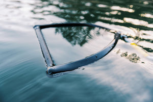 Black handle of the Ski Rope & Handle Combo floating on water, partially submerged with reflections.