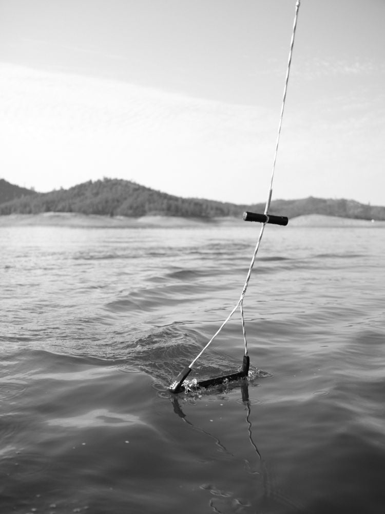 Black and white Wake Rope and T-Bar Handle floating on the water by a lake.