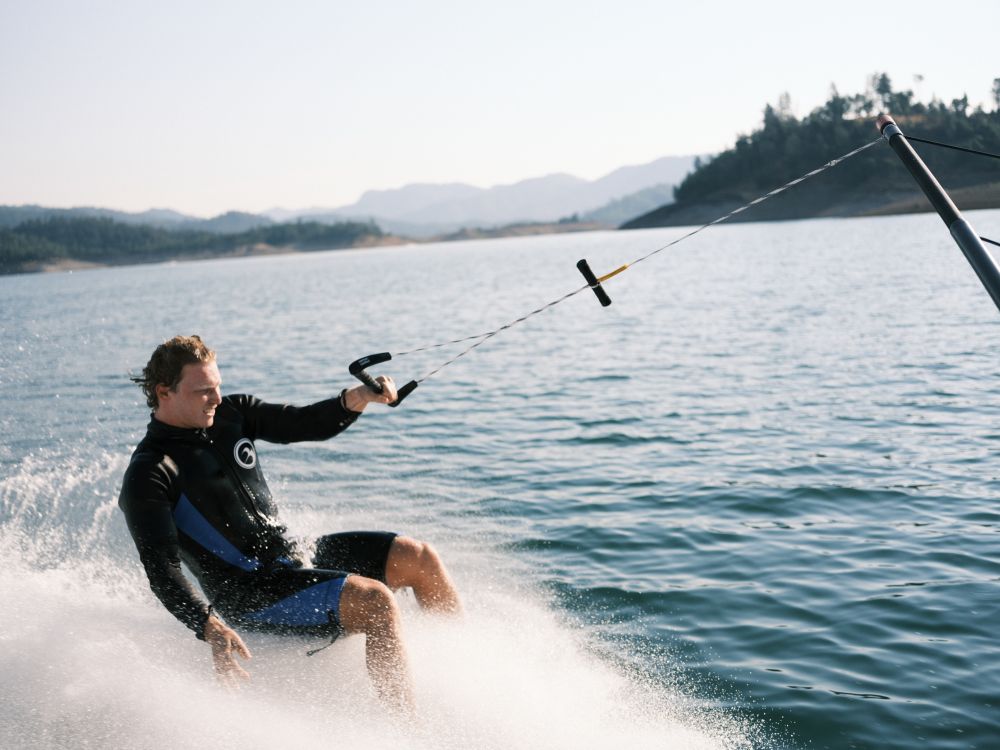 Man in a wetsuit barefoot skiing while holding the Wake Rope and T-Bar Handle.