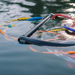Black handle floating on water, surrounded by loops of multicolored ski rope.
