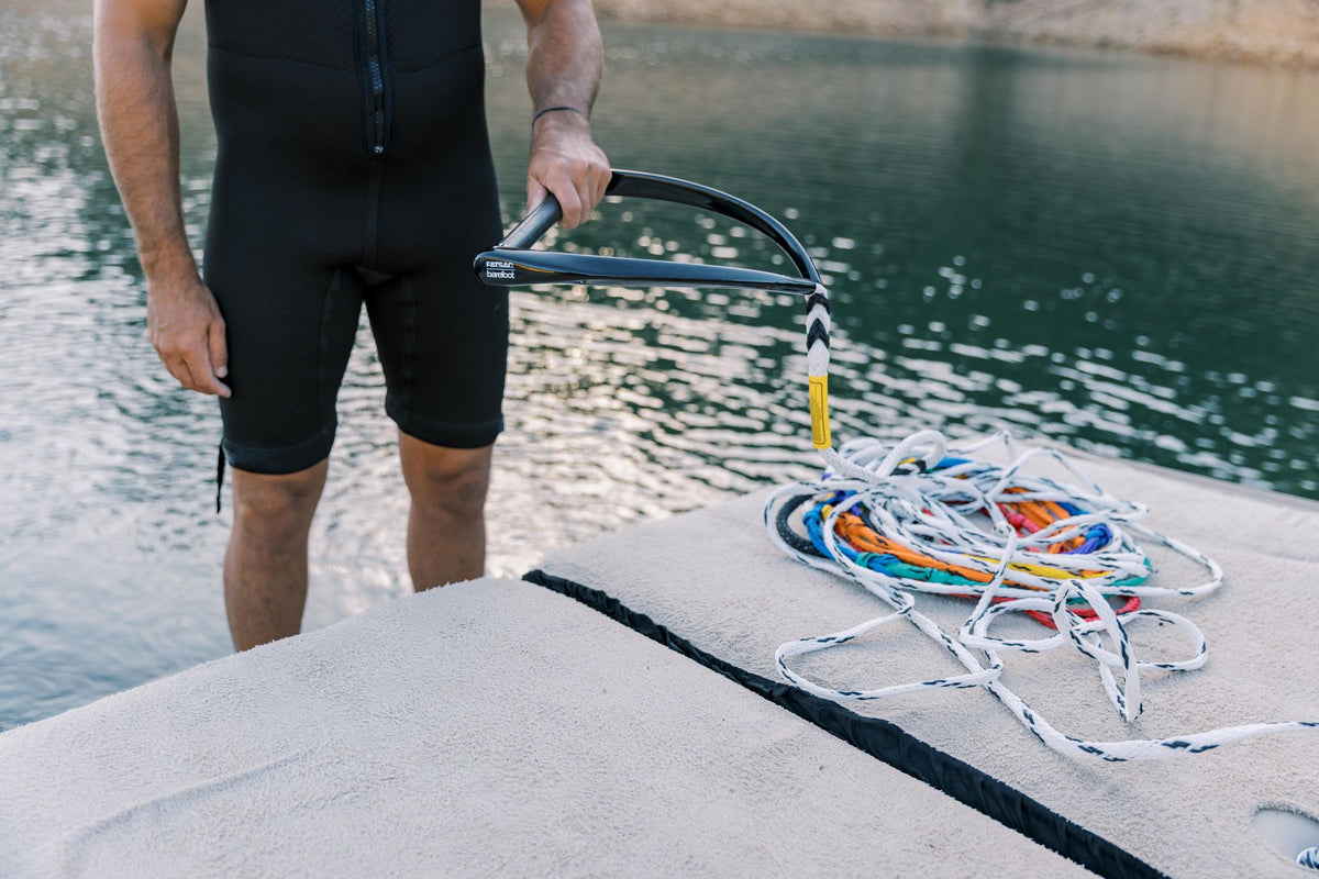 Person in a wetsuit standing on a dock, holding the black handle with a coiled multicolored rope beside them.