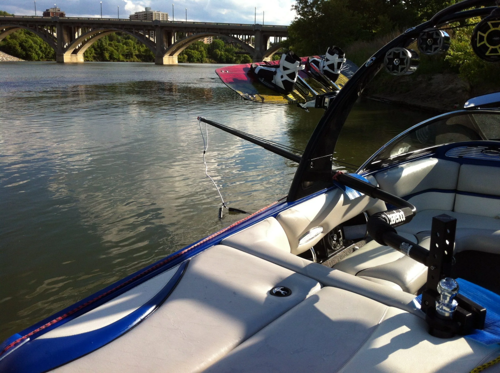 Deluxe Quad V-Drive Boom mounted on a boat with a wakeboard, near a bridge.