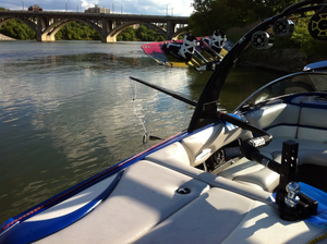 Deluxe Quad V-Drive Boom mounted on a boat with a wakeboard, near a bridge.